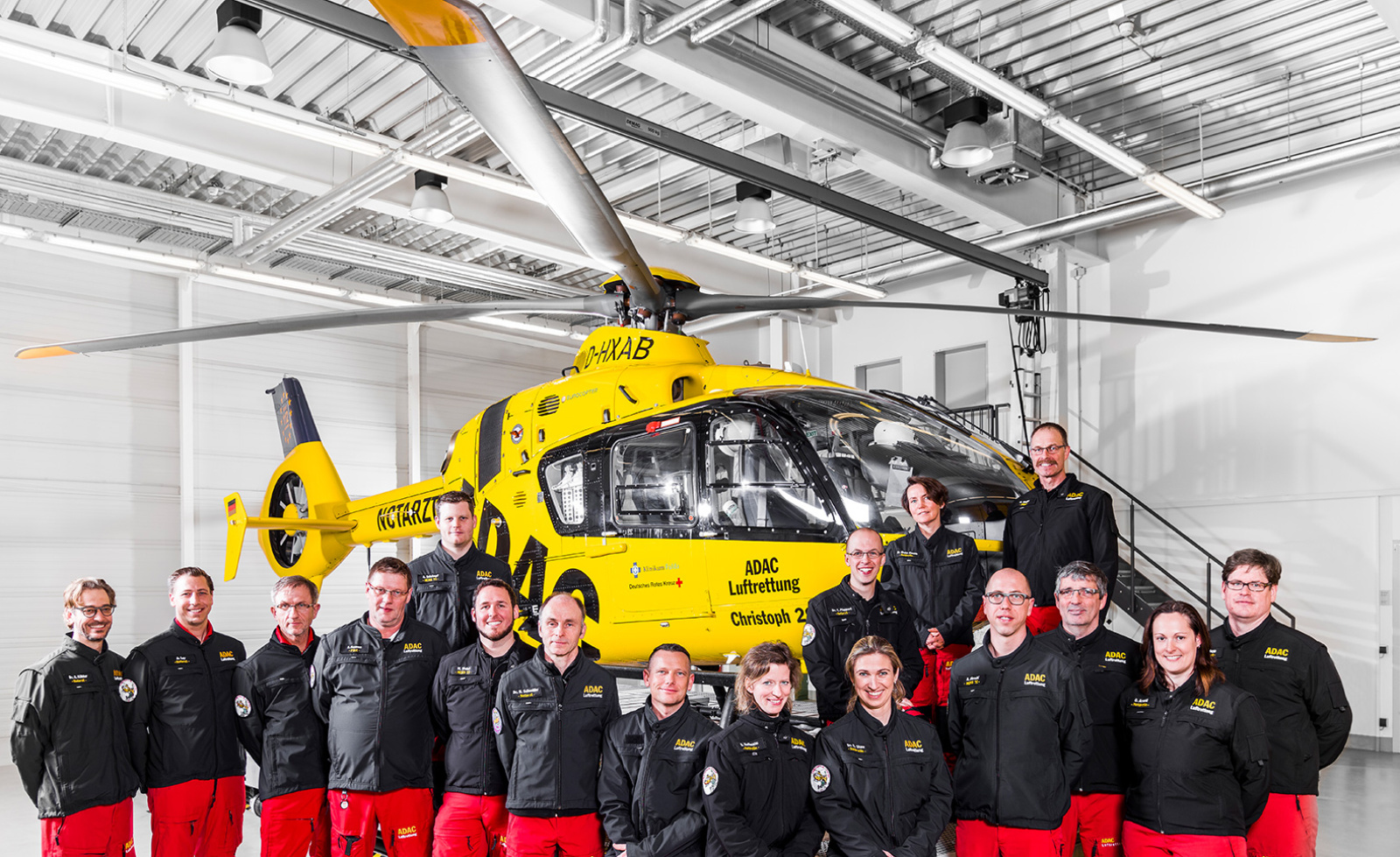 Crew der ADAC Luftrettung posiert vor gelbem Rettungshubschrauber im Hangar.