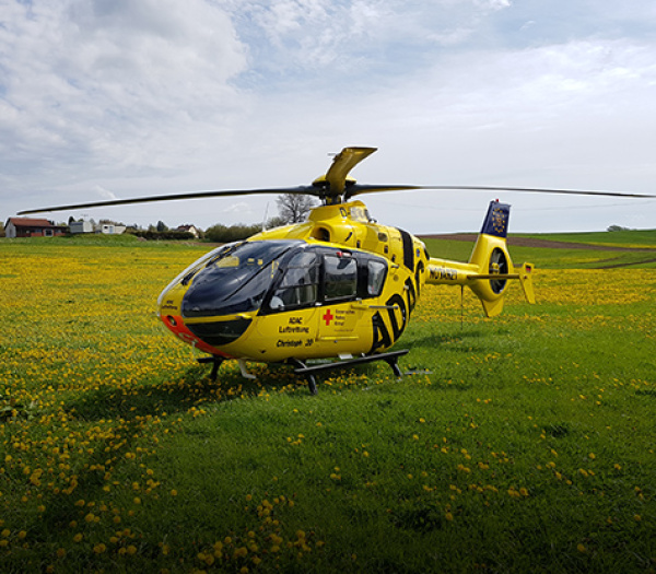 ADAC Luftrettung Rettungshubschrauber auf blühender Wiese mit Löwenzahn vor ländlicher Kulisse.