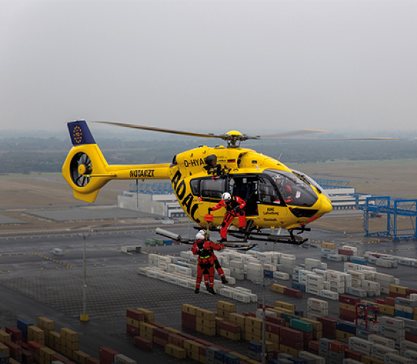 ADAC Luftrettung Rettungshubschrauber setzt per Winde zwei Rettungskräfte über Containerterminal ab.