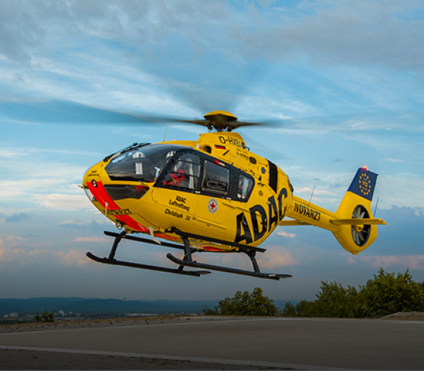 Rettungshubschrauber der ADAC Luftrettung mit Besatzung schwebt über Landeplatz bei Dämmerung
