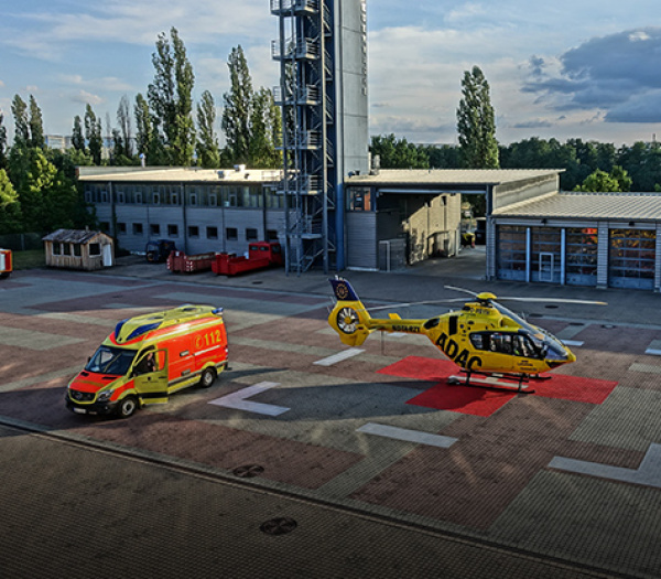 ADAC Luftrettung-Rettungshubschrauber steht neben Rettungswagen auf Landeplatz vor Einsatzgebäude