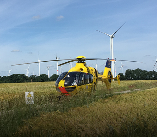 Gelber ADAC Luftrettung Rettungshubschrauber auf Feldweg gelandet, Windräder im Hintergrund.