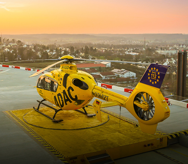 Rettungshubschrauber der ADAC Luftrettung steht auf Krankenhaus-Helipad bei Sonnenuntergang.