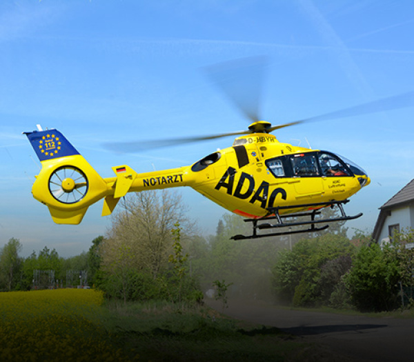 Gelber ADAC Rettungshubschrauber der ADAC Luftrettung mit NOTARZT-Aufschrift landet über Dorfwiese, Staub aufgewirbelt.