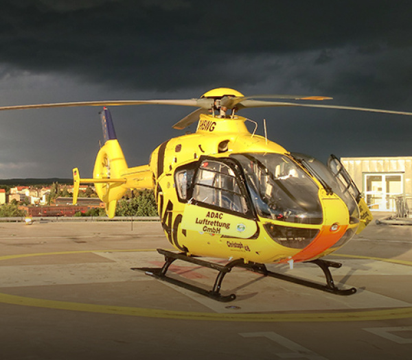 Gelber ADAC Luftrettung Rettungshubschrauber auf dem Landeplatz bei dunklem Gewitterhimmel.