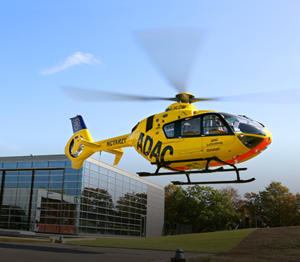 Rettungshubschrauber der ADAC Luftrettung im Landeanflug vor einem Gebäude, Besatzung im Cockpit sichtbar