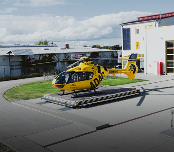 Gelber ADAC Luftrettung Rettungshubschrauber auf Startplattform vor Hangar, bereit für Einsätze