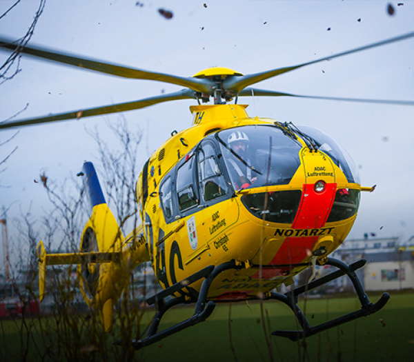 ADAC Luftrettung Rettungshubschrauber beim Landen auf Feld, Besatzung im Cockpit sichtbar