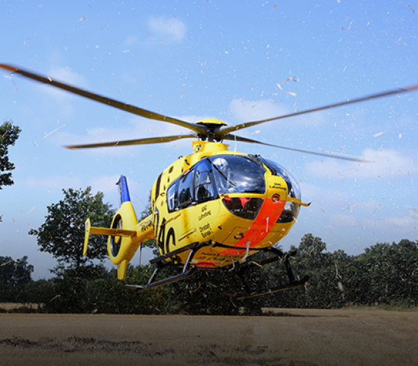 ADAC Luftrettung Rettungshubschrauber schwebt bodennah über ein Feld und wirbelt beim Absetzen Staub auf.