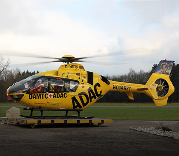 Gelber Rettungshubschrauber der ADAC Luftrettung mit Notarztbesatzung steht am Boden auf Startplattform.