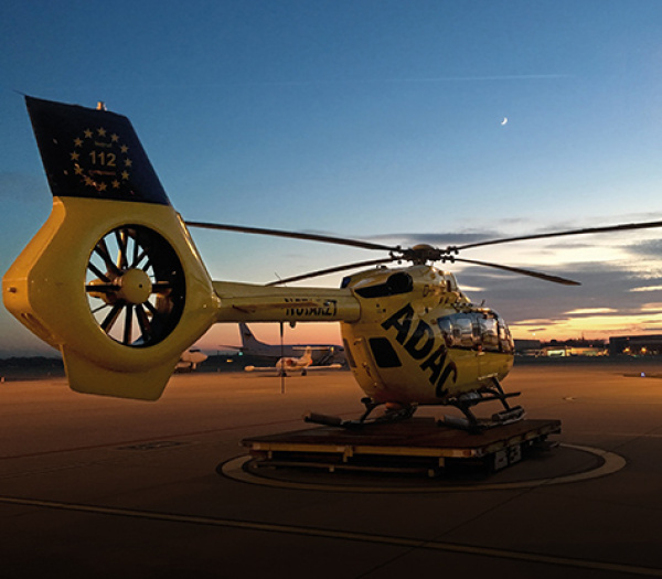 ADAC Luftrettung Rettungshubschrauber steht bei Dämmerung auf Startplatz am Flughafen.