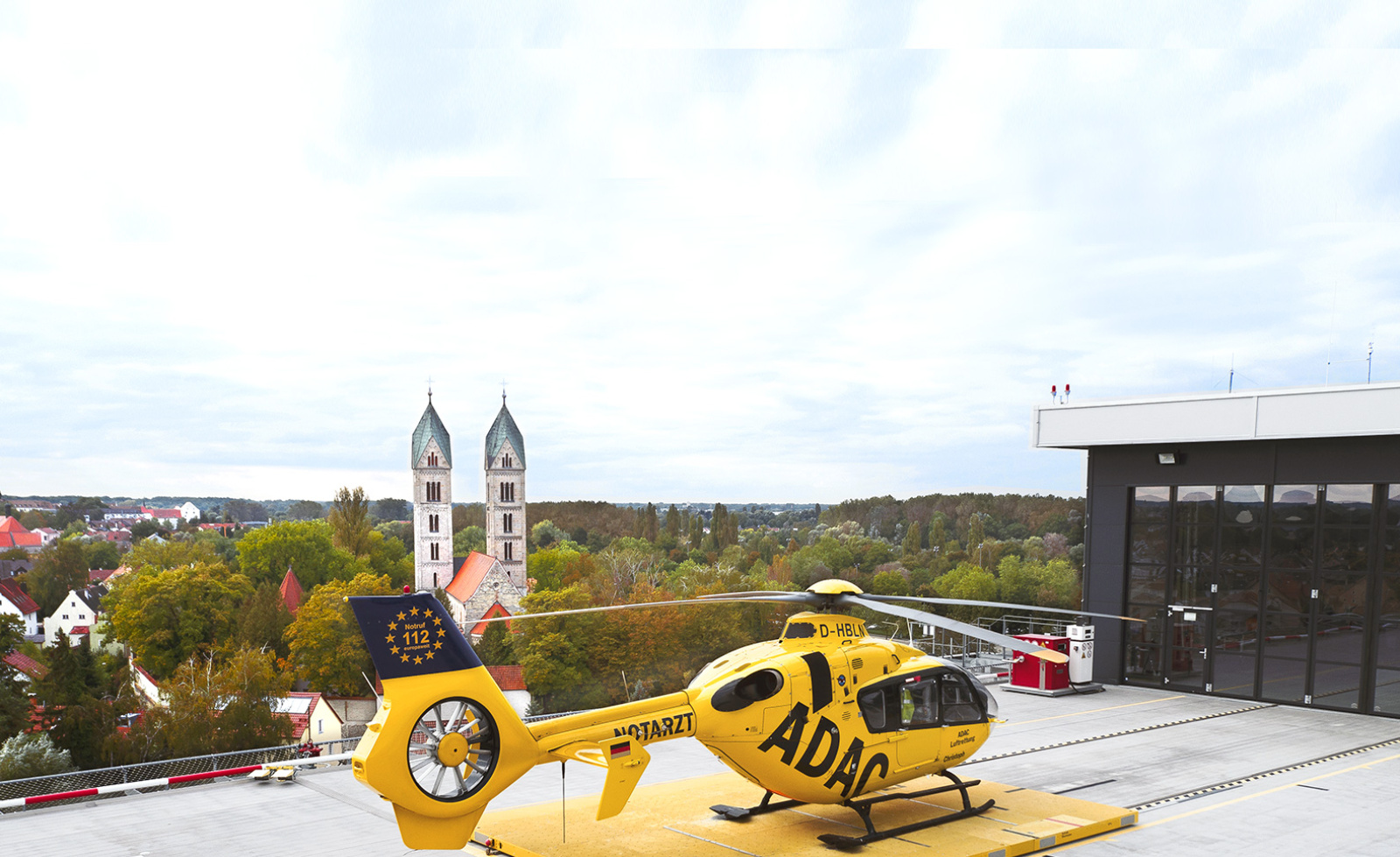 ADAC Rettungshubschrauber auf Krankenhaus-Helipad der ADAC Luftrettung vor Stadtkulisse mit Kirchtürmen.