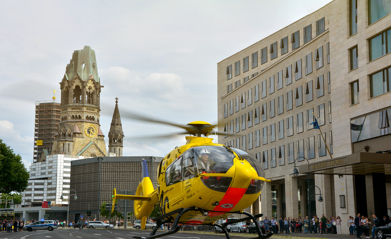 ADAC Luftrettung‑Rettungshubschrauber landet vor Gedächtniskirche; Polizei und Schaulustige an der Straße.