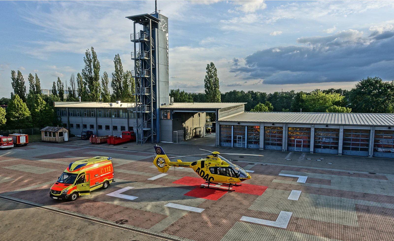 ADAC Luftrettung gelber Rettungshubschrauber auf Landeplatz vor Feuerwache, daneben Rettungswagen mit 112.