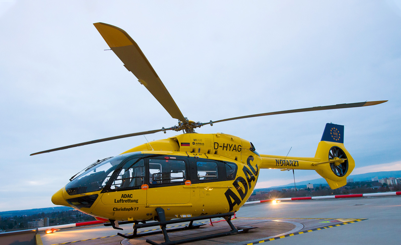 Gelber ADAC Luftrettung Rettungshubschrauber Christoph 77 auf Dach-Heliport, bereit für Notfalleinsätze.