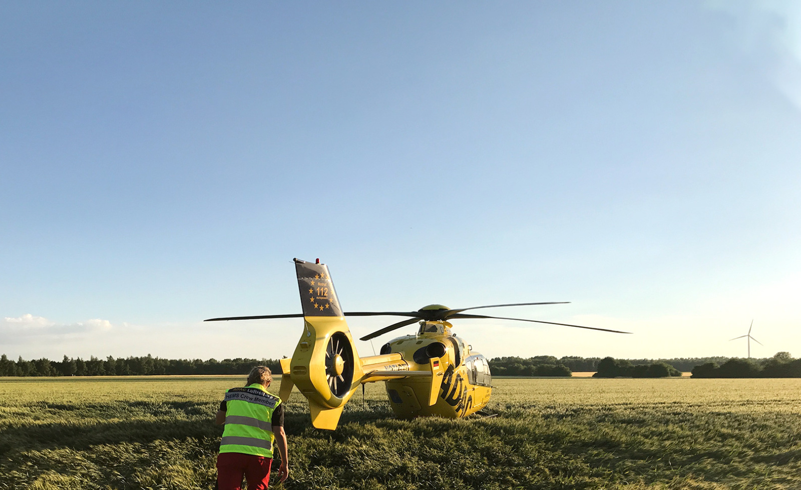 ADAC Luftrettung-Rettungshubschrauber gelandet auf Feld, Crew-Mitglied in Warnweste nähert sich dem gelben Hubschrauber