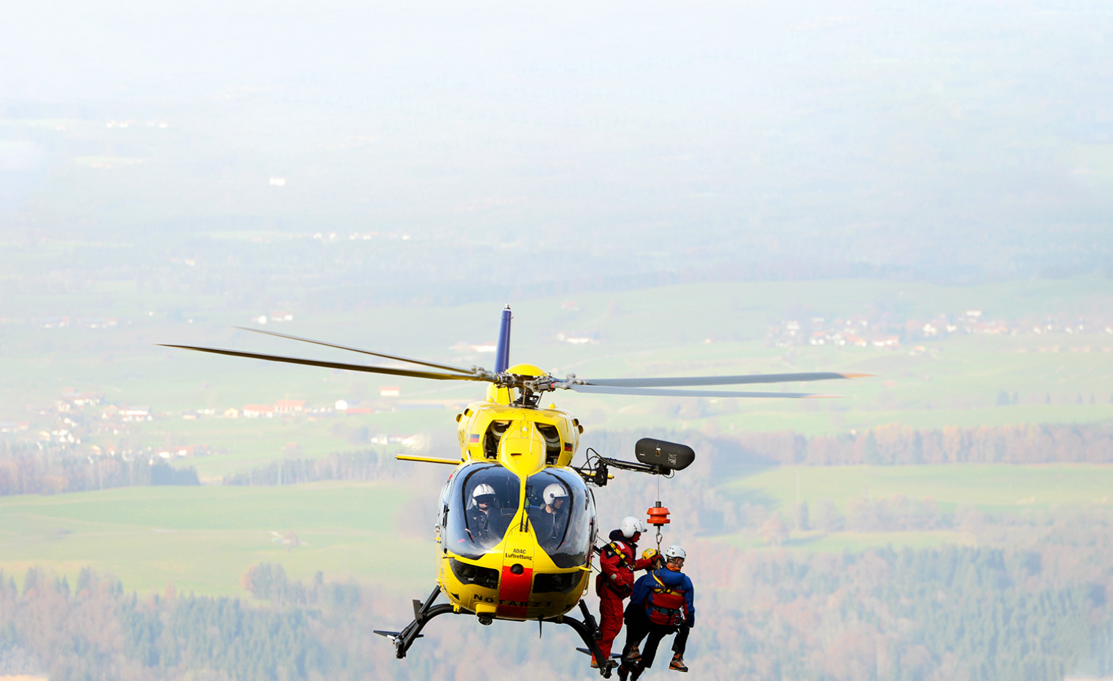 ADAC Luftrettung Rettungshubschrauber mit Rettungskräften bei Seilbergung über ländlicher Landschaft