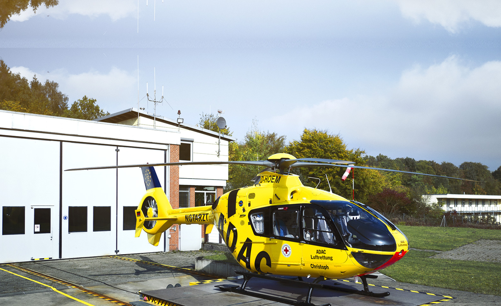 Gelber Rettungshubschrauber der ADAC Luftrettung steht auf Landeplatz vor Rettungsstation.