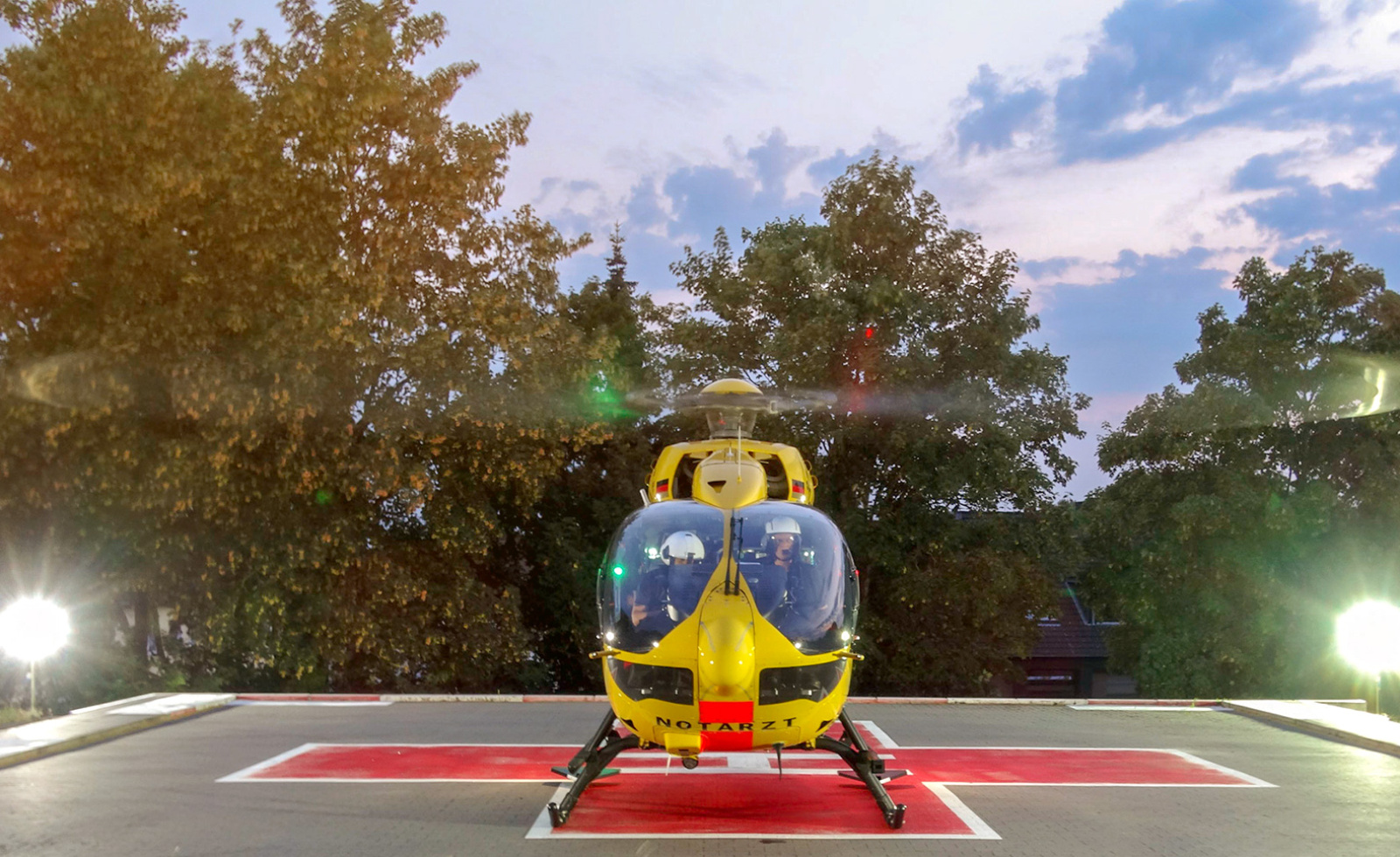 Gelber Rettungshubschrauber der ADAC Luftrettung mit Besatzung auf Helipad bei Abenddämmerung.