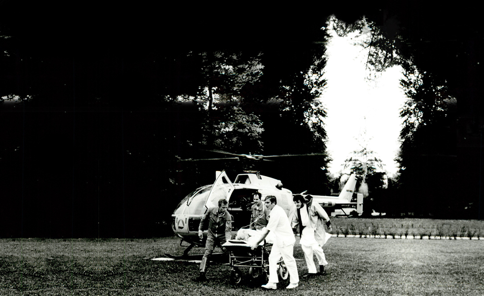 ADAC Luftrettung Rettungshubschrauber gelandet, Besatzung und Rettungskräfte schieben Trage mit Patient über Wiese.