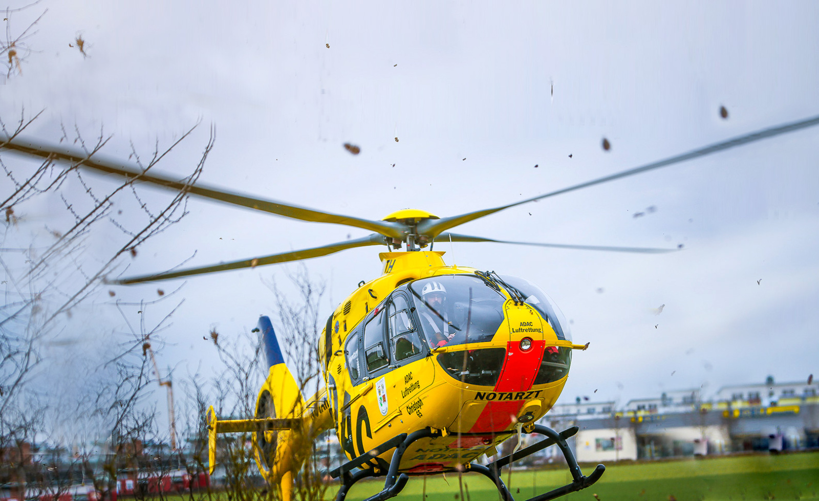 Gelber Rettungshubschrauber der ADAC Luftrettung beim Start über Feld, Pilot im Cockpit sichtbar.