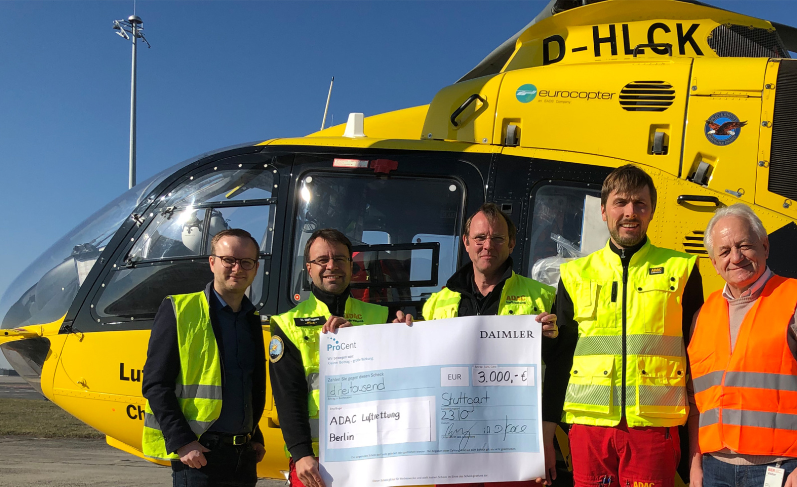 Fünf Personen vor gelbem Rettungshubschrauber halten Scheck über 3.000 Euro an ADAC Luftrettung Berlin.