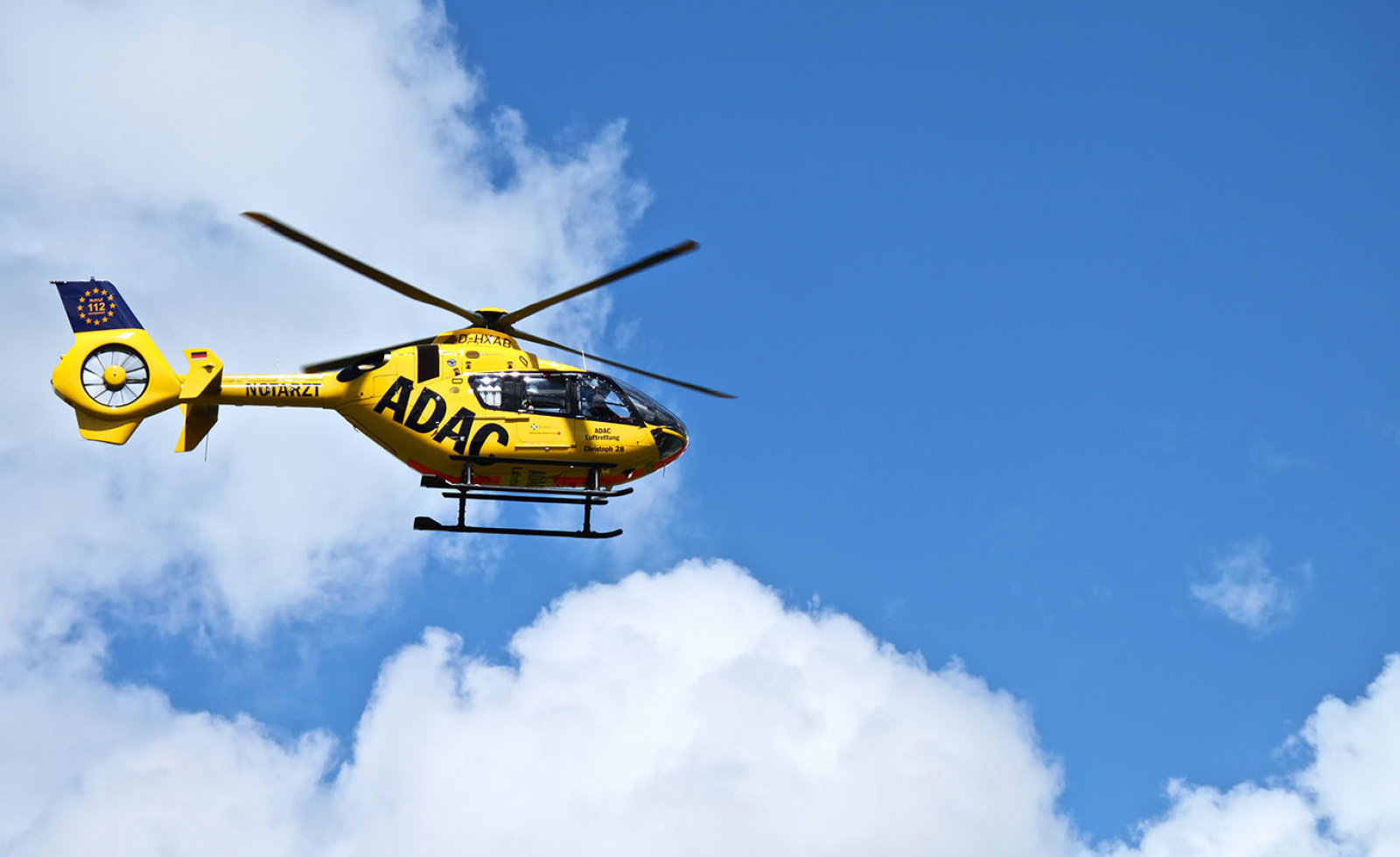 Gelber Rettungshubschrauber der ADAC Luftrettung im Flug über Wolken, Besatzung einsatzbereit.