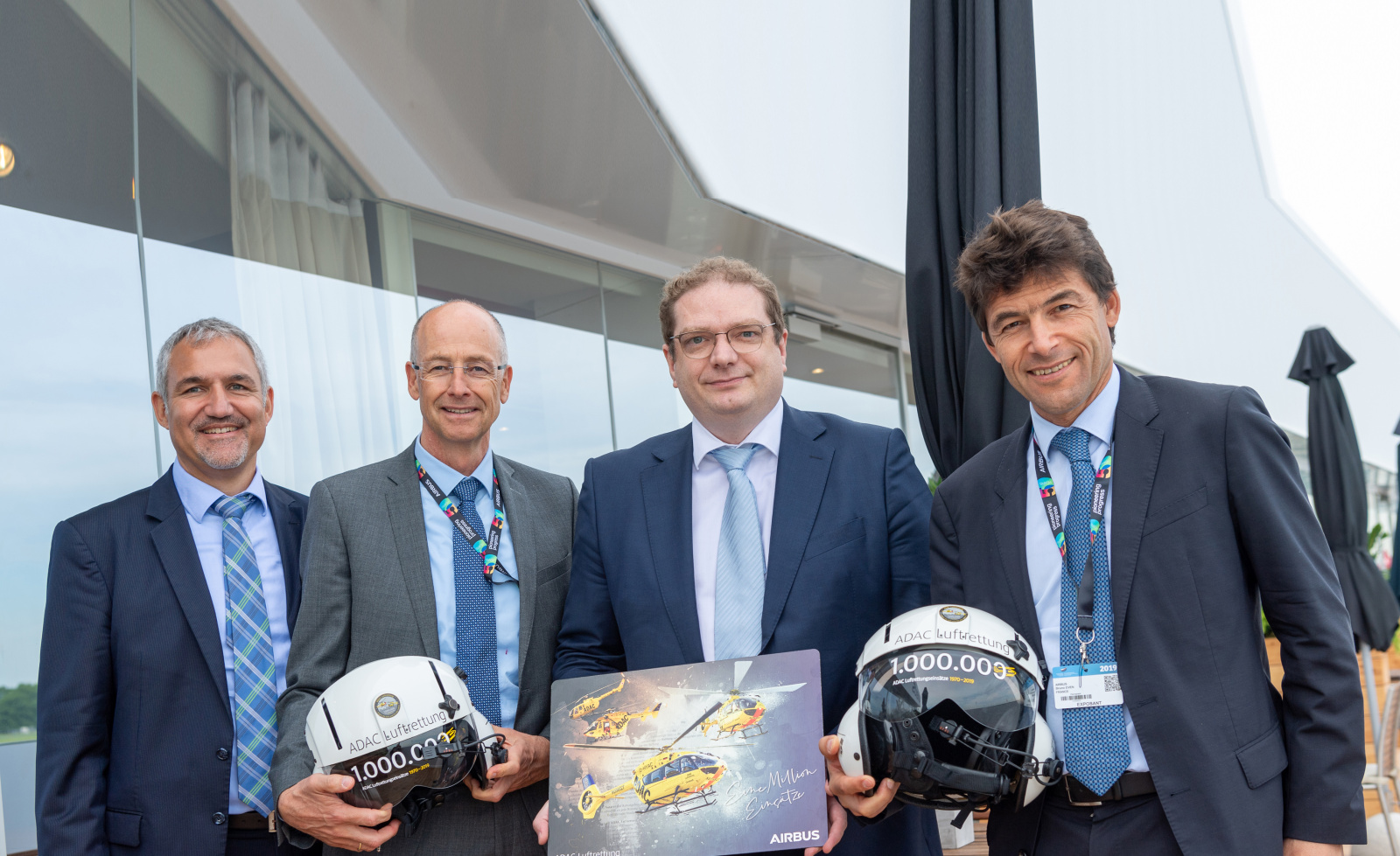 Vier Männer in Anzügen präsentieren ADAC Luftrettung-Helme und eine Airbus-Tafel mit gelben Rettungshubschraubern.