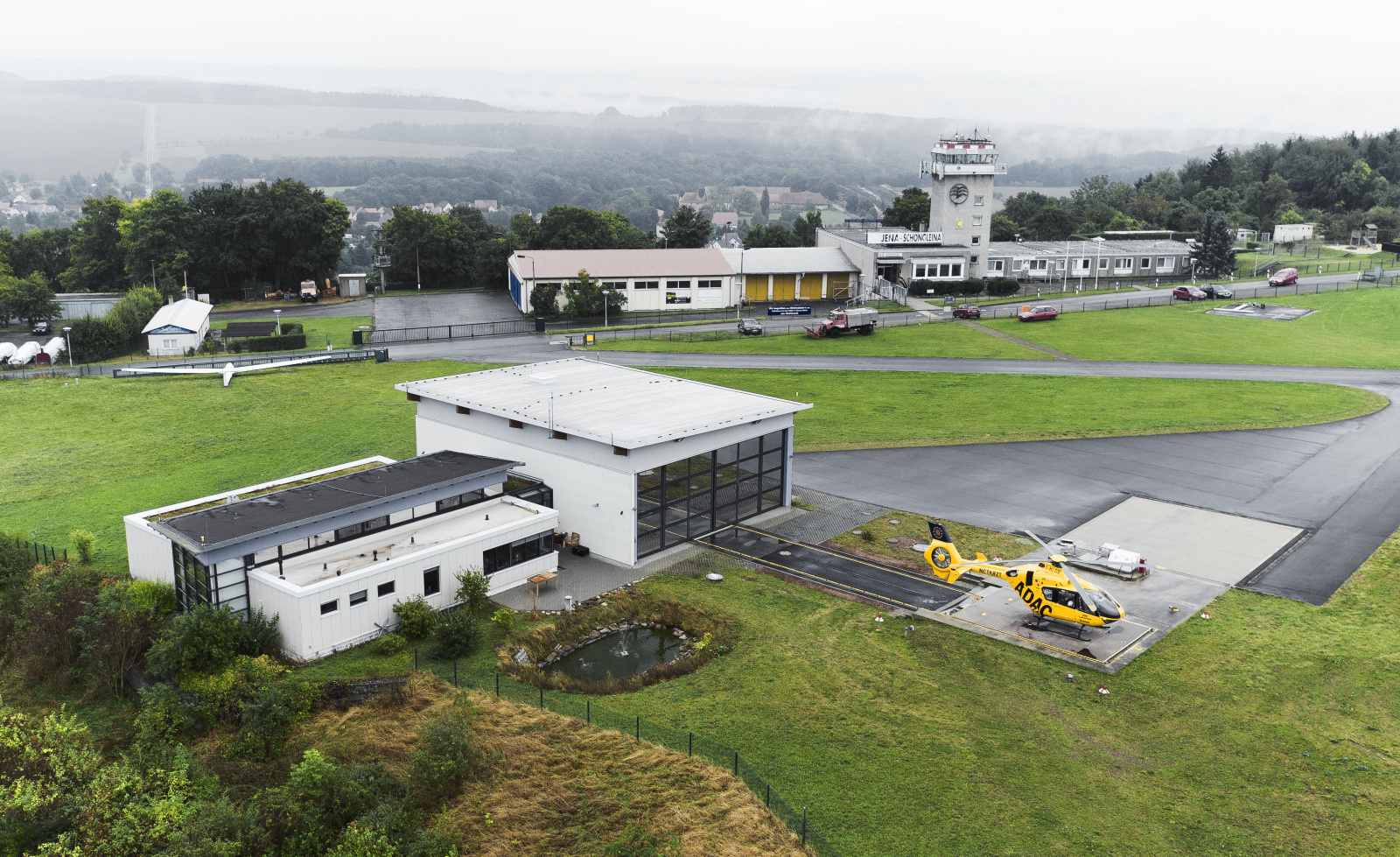 ADAC Luftrettung-Rettungshubschrauber auf Startplatz neben Hangar und Tower an kleinem Flugplatz