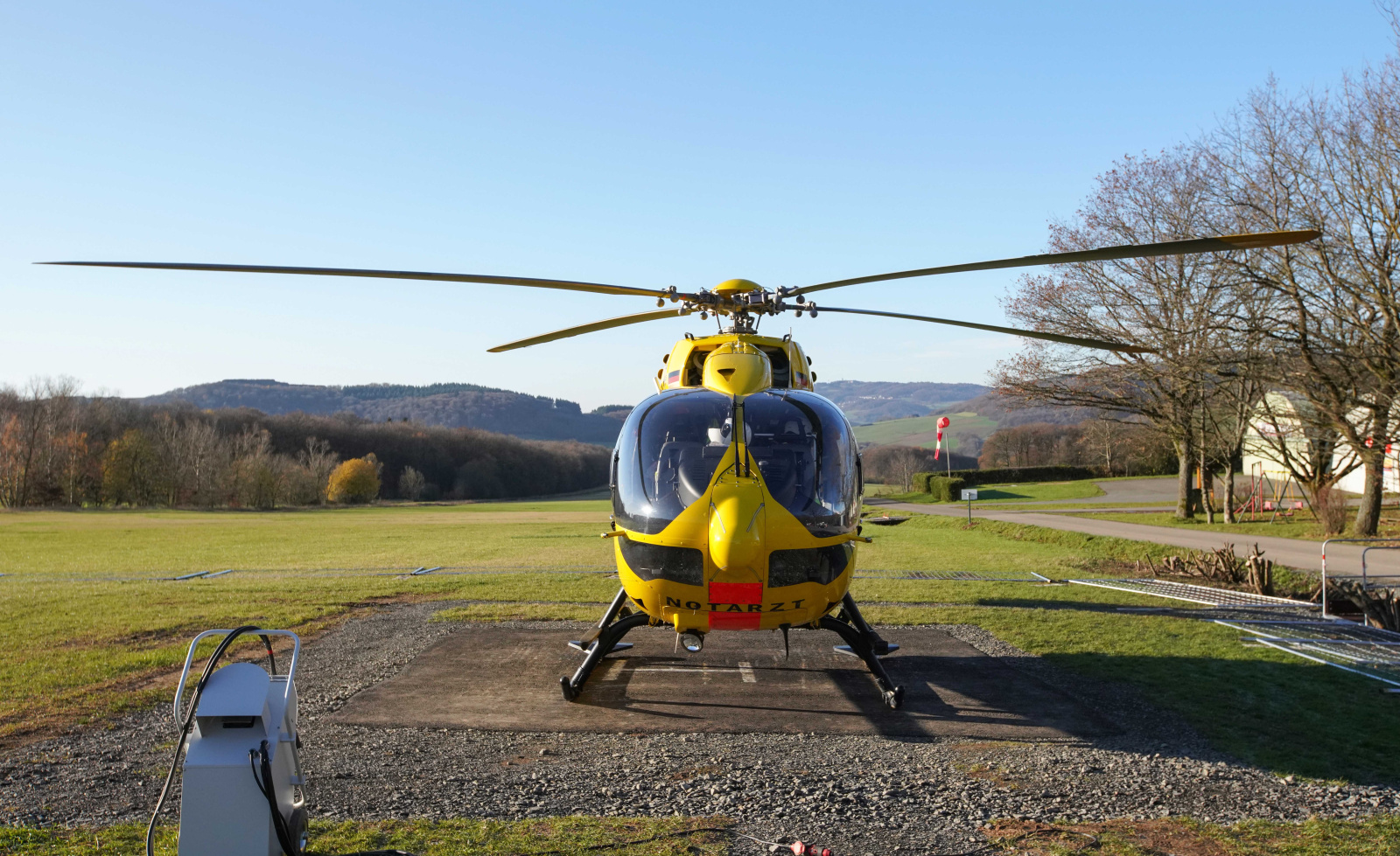 Gelber Rettungshubschrauber der ADAC Luftrettung auf Landeplatz vor ländlicher Kulisse.