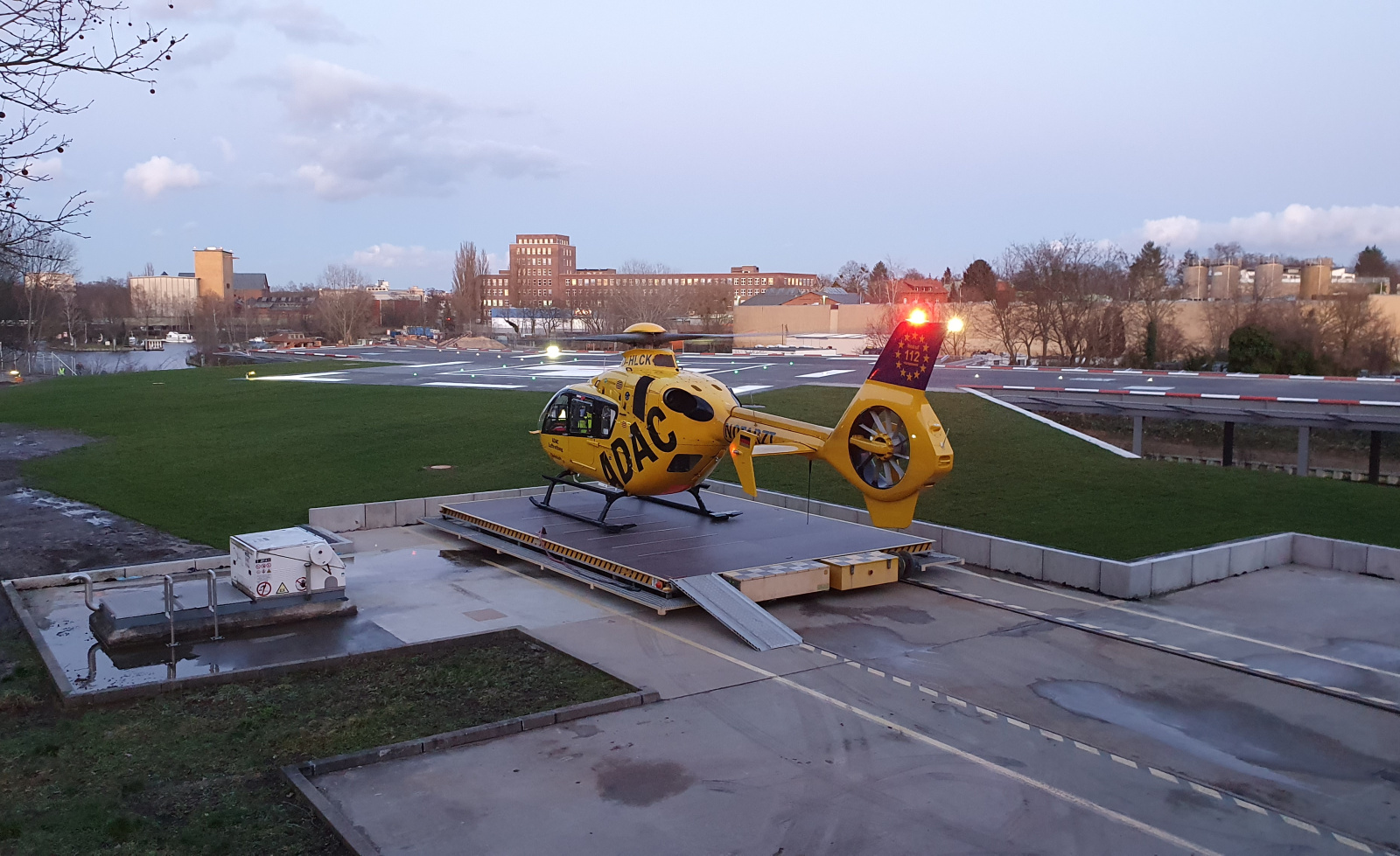 ADAC Luftrettung Rettungshubschrauber auf Landeplattform bei Dämmerung vor städtischer Kulisse