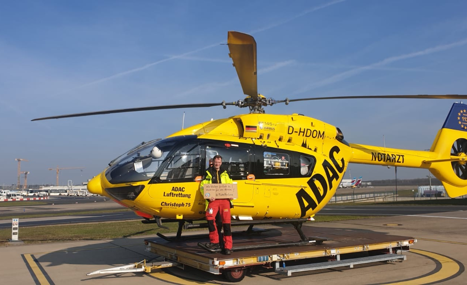 ADAC Luftrettung Rettungshubschrauber "Christoph 75" am Flughafen, Besatzungsmitglied in Uniform steht davor.
