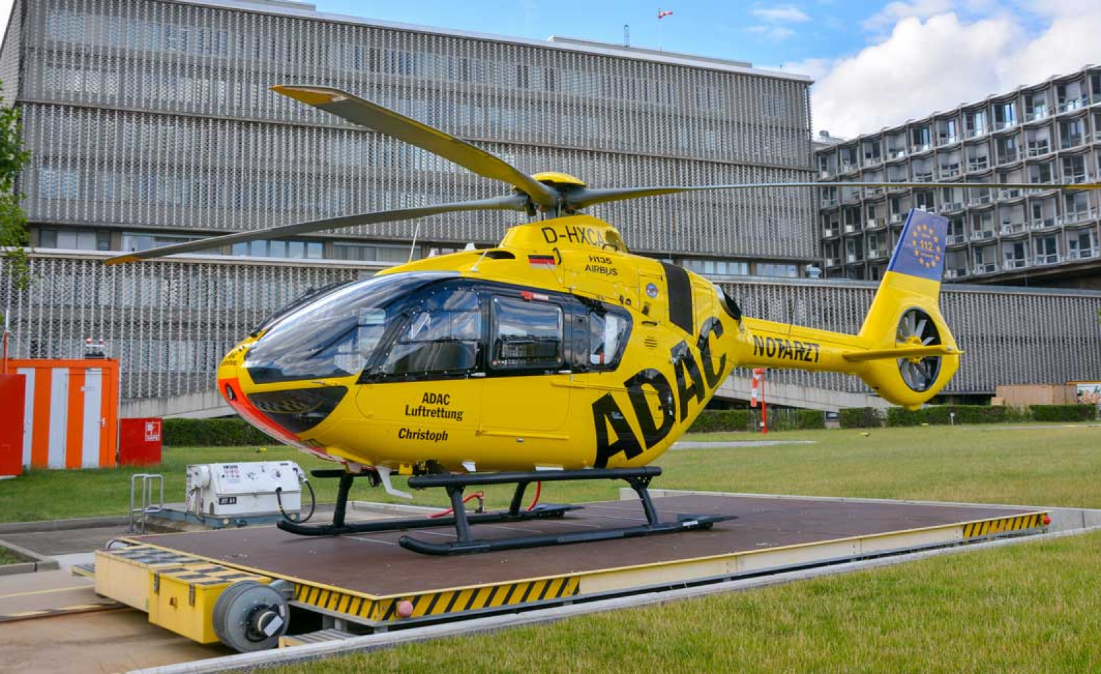 ADAC Luftrettung Rettungshubschrauber Christoph steht auf Landeplattform vor Klinikgebäude.