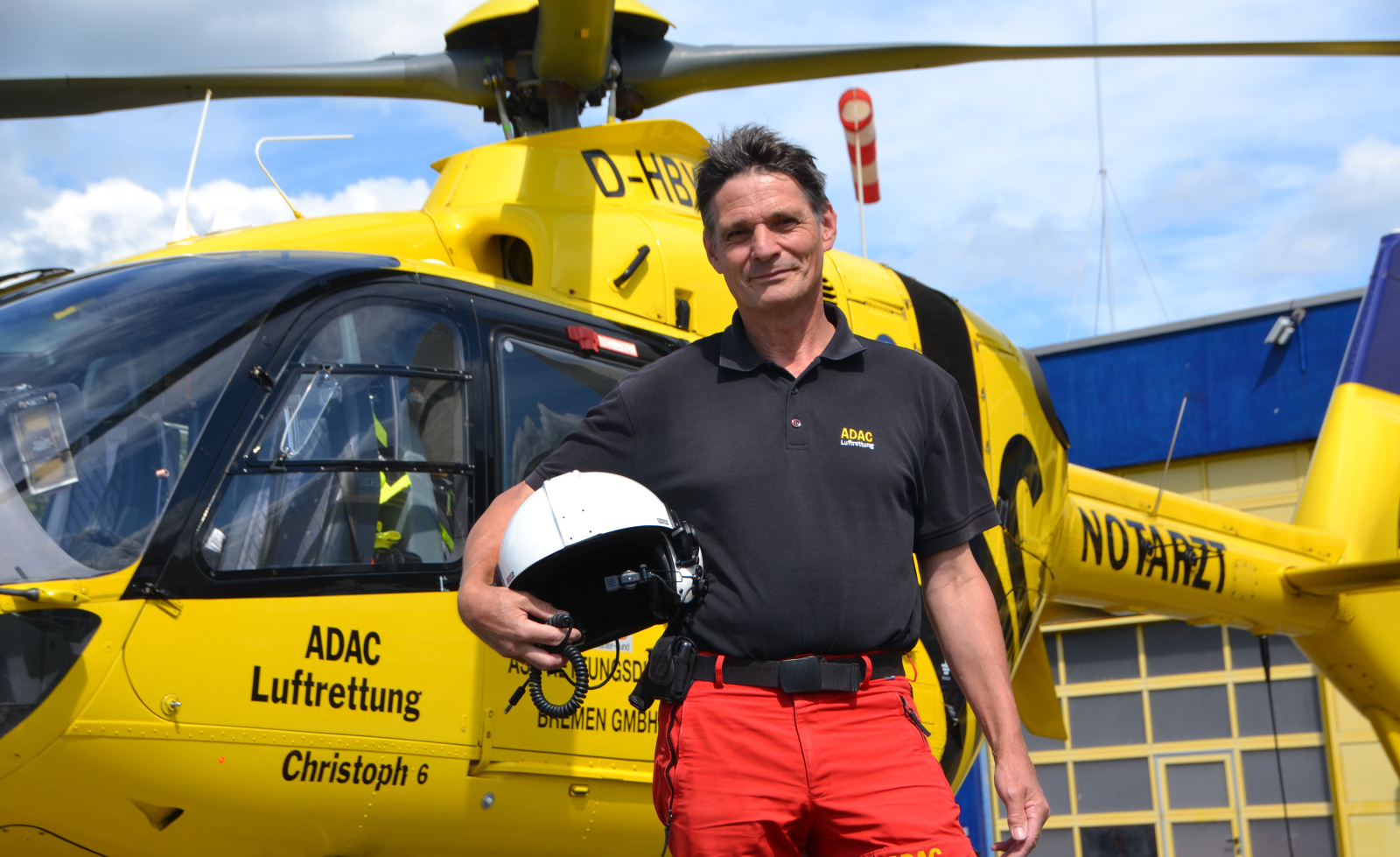ADAC Luftrettung-Crewmitglied in Uniform mit Helm vor gelbem Rettungshubschrauber Christoph 6.