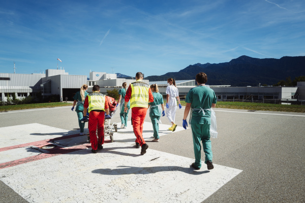 ADAC Luftrettung und Klinikteam schieben Patienten auf Trage über Landeplatz zur Versorgung.